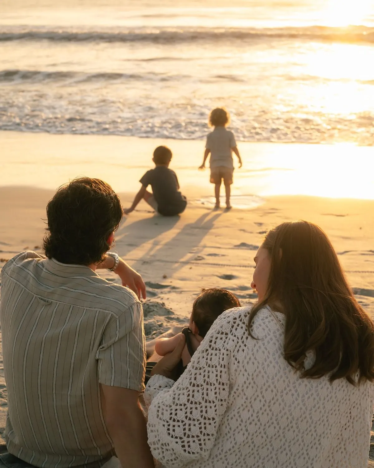 A family sitting together at the water's edge at sunset